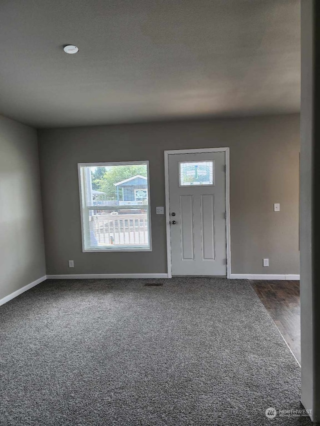 entrance foyer with baseboards and dark colored carpet