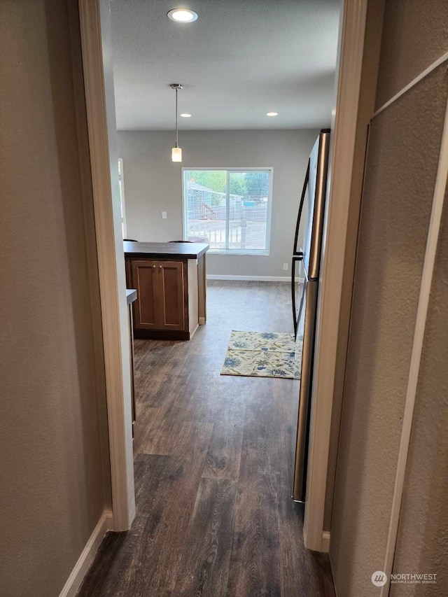 hall featuring dark wood-type flooring, recessed lighting, and baseboards