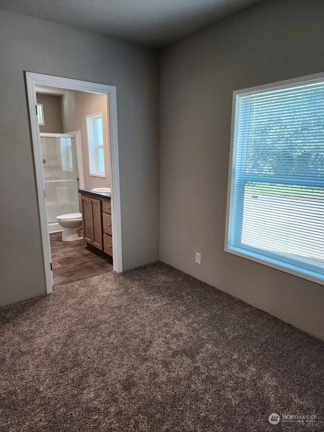 unfurnished bedroom featuring dark carpet and ensuite bath