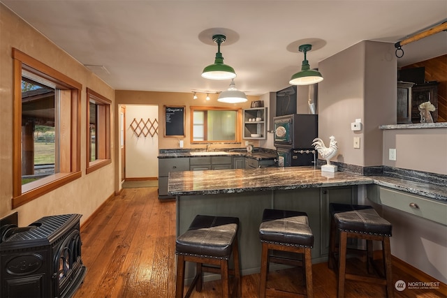 kitchen featuring hardwood / wood-style flooring, dark stone counters, a kitchen bar, gray cabinets, and hanging light fixtures