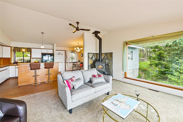 living room with a wealth of natural light, lofted ceiling, a wood stove, and ceiling fan with notable chandelier