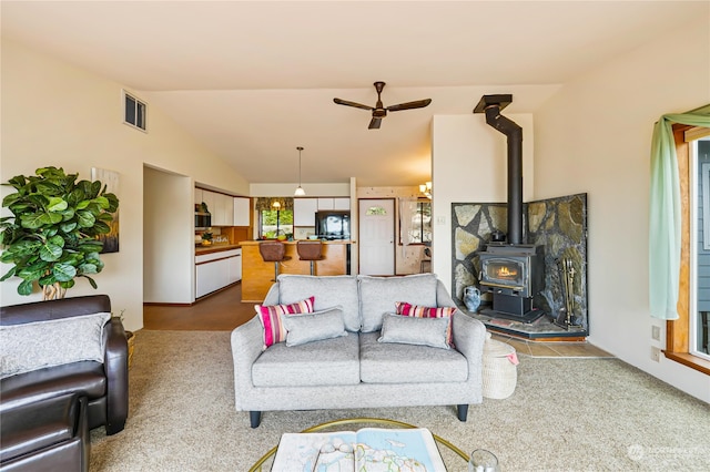 carpeted living room with vaulted ceiling, ceiling fan, and a wood stove