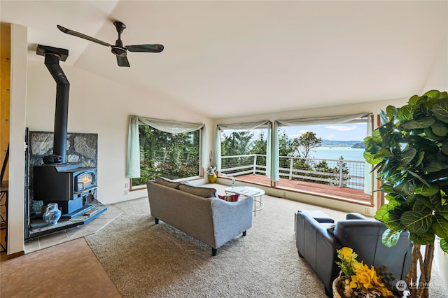 living room featuring a water view, carpet, a wood stove, ceiling fan, and lofted ceiling