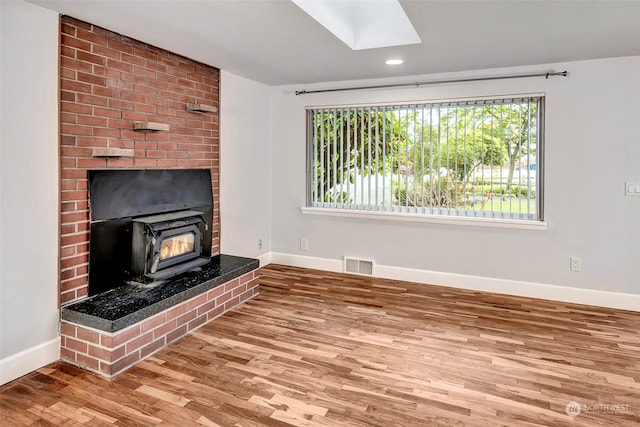 unfurnished living room with brick wall, a skylight, a wood stove, and light wood-type flooring