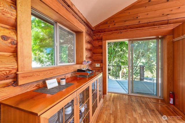 doorway with log walls, light hardwood / wood-style floors, vaulted ceiling, and a wealth of natural light