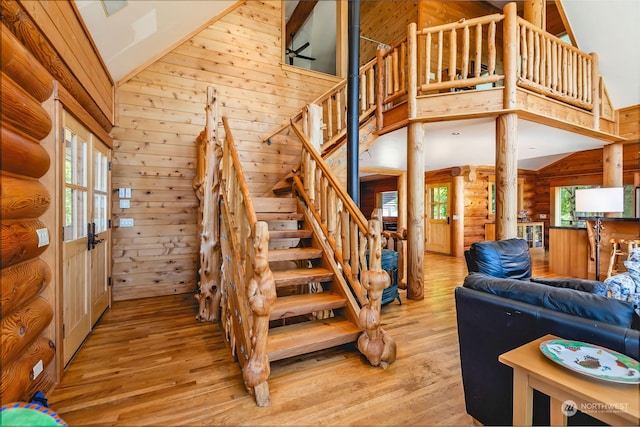 staircase featuring high vaulted ceiling, wood walls, light hardwood / wood-style flooring, and ornate columns