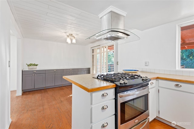 kitchen featuring light hardwood / wood-style floors, kitchen peninsula, gray cabinetry, island exhaust hood, and stainless steel gas stove