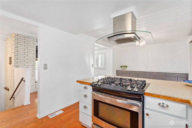 kitchen featuring stainless steel gas range oven, island exhaust hood, light hardwood / wood-style flooring, and white cabinetry