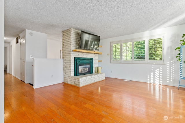 unfurnished living room featuring brick wall, light wood-type flooring, a fireplace, and a textured ceiling