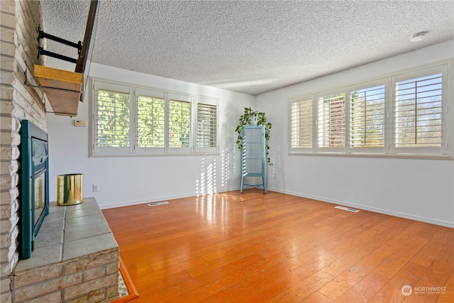 unfurnished living room featuring brick wall, a brick fireplace, light hardwood / wood-style flooring, and a textured ceiling