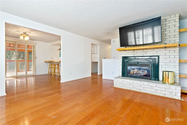 unfurnished living room with a brick fireplace, brick wall, a textured ceiling, and light wood-type flooring