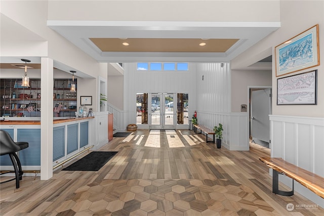 foyer featuring french doors, light hardwood / wood-style flooring, a tray ceiling, and a towering ceiling