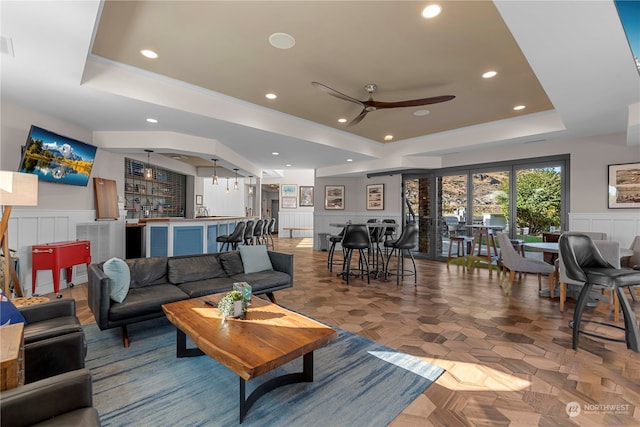 living room featuring a raised ceiling, parquet floors, and ceiling fan