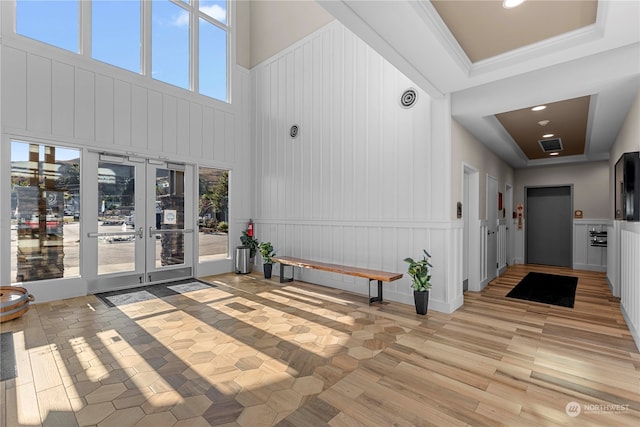 interior space featuring a high ceiling, light hardwood / wood-style floors, french doors, and a raised ceiling