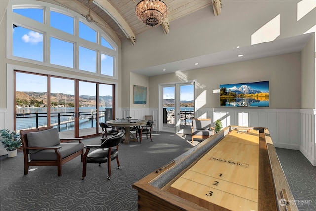 game room with a water view, dark carpet, high vaulted ceiling, and a chandelier