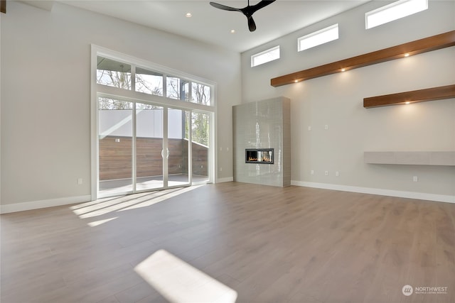 unfurnished living room with a tiled fireplace, light hardwood / wood-style floors, ceiling fan, and a high ceiling