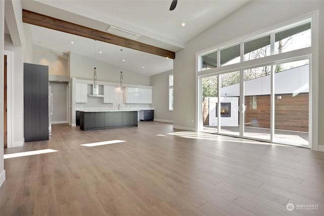 unfurnished living room featuring ceiling fan, light wood-type flooring, beam ceiling, and high vaulted ceiling