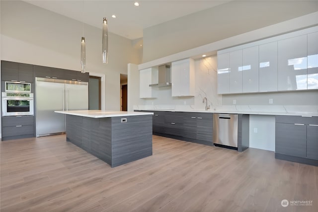 kitchen featuring built in appliances, light hardwood / wood-style floors, a kitchen island, wall chimney exhaust hood, and white cabinets