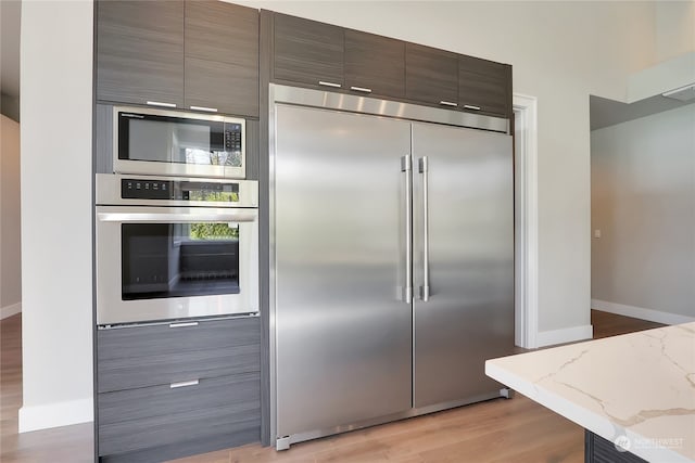 kitchen featuring built in appliances, light hardwood / wood-style floors, and light stone countertops