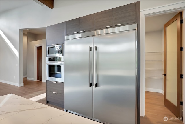 kitchen with built in appliances, light hardwood / wood-style flooring, and beamed ceiling