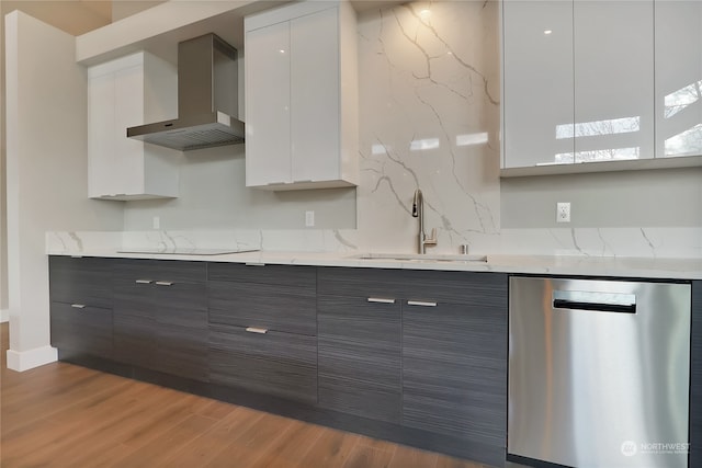 kitchen with hardwood / wood-style floors, wall chimney range hood, light stone counters, dishwasher, and sink