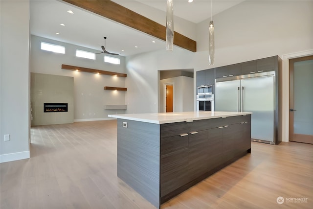 kitchen featuring built in appliances, light wood-type flooring, a center island, and a large fireplace