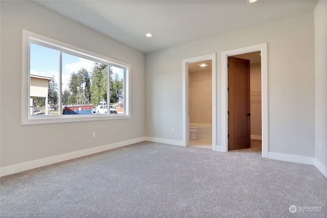 unfurnished bedroom featuring a spacious closet, ensuite bathroom, light carpet, and a closet