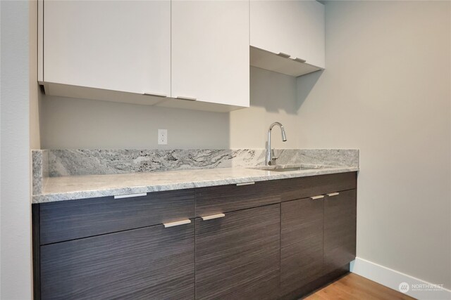 interior space featuring light stone countertops, light hardwood / wood-style flooring, white cabinets, dark brown cabinetry, and sink