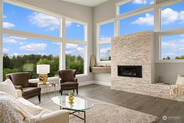 living room with dark hardwood / wood-style flooring, a stone fireplace, plenty of natural light, and a high ceiling