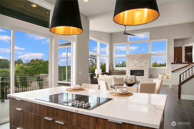 kitchen with light stone counters, dark hardwood / wood-style floors, black electric cooktop, a center island, and a fireplace