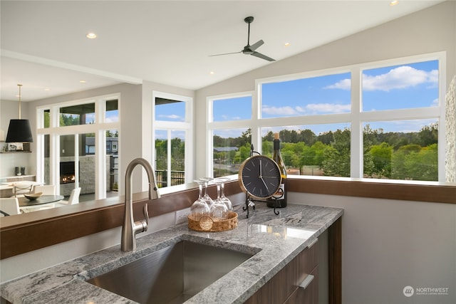 interior space featuring vaulted ceiling, ceiling fan, hanging light fixtures, light stone counters, and sink