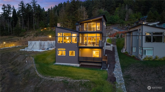 back house at dusk featuring a balcony and a yard