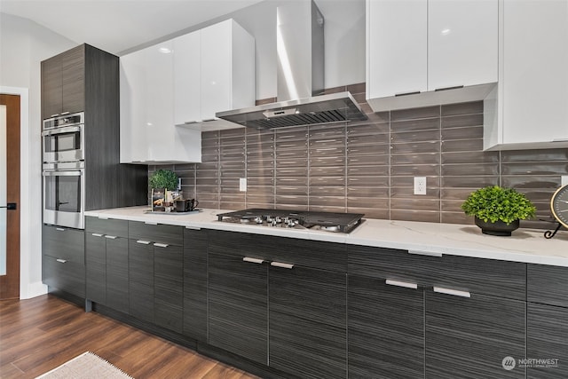 kitchen with decorative backsplash, appliances with stainless steel finishes, wall chimney range hood, dark hardwood / wood-style floors, and white cabinetry