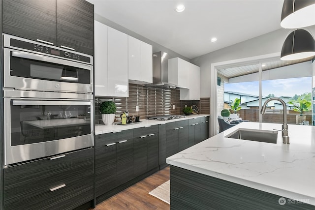 kitchen featuring sink, wall chimney range hood, decorative light fixtures, white cabinets, and appliances with stainless steel finishes