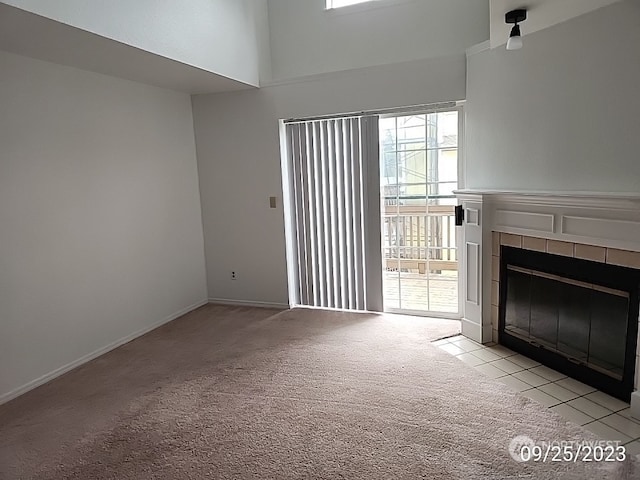 unfurnished living room with a tiled fireplace, light carpet, a wealth of natural light, and a high ceiling