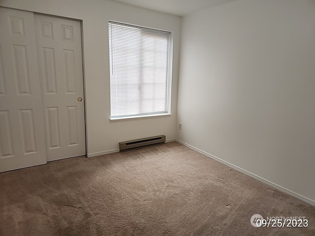 unfurnished bedroom featuring carpet flooring, baseboard heating, and a closet