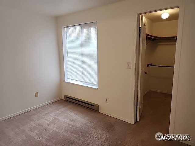 unfurnished bedroom featuring dark carpet, a walk in closet, a closet, and baseboard heating