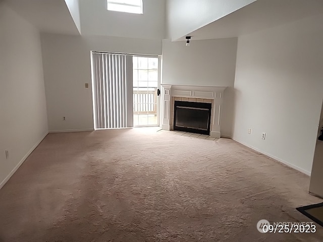 unfurnished living room with light carpet, a towering ceiling, and a tiled fireplace