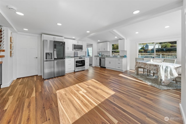 kitchen featuring appliances with stainless steel finishes, light stone counters, white cabinets, wood-type flooring, and lofted ceiling with beams