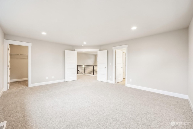 unfurnished bedroom featuring ensuite bath, light colored carpet, a walk in closet, and a closet