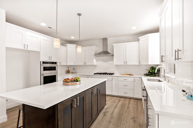 kitchen with a center island, wall chimney range hood, sink, appliances with stainless steel finishes, and decorative light fixtures