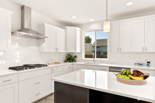 kitchen with pendant lighting, white cabinets, sink, wall chimney exhaust hood, and stainless steel appliances