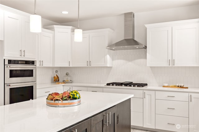 kitchen with white cabinets, decorative light fixtures, stainless steel appliances, and wall chimney range hood