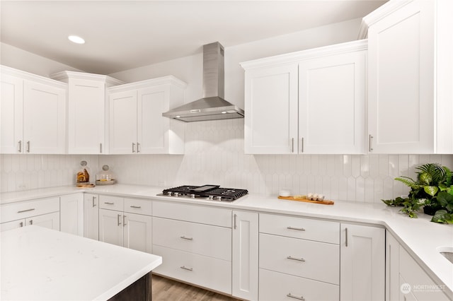 kitchen with tasteful backsplash, white cabinets, wall chimney range hood, and stainless steel gas stovetop