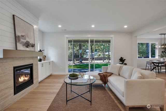 living area with light wood finished floors, recessed lighting, an inviting chandelier, a tile fireplace, and baseboards