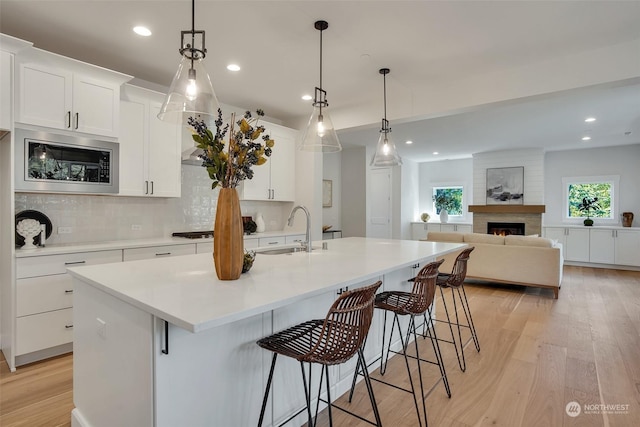 kitchen featuring light countertops, an island with sink, a sink, and white cabinets