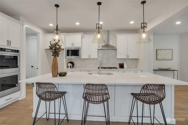 kitchen featuring hanging light fixtures, wall chimney range hood, stainless steel appliances, and light countertops