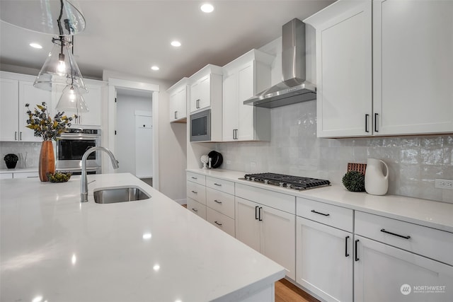 kitchen featuring wall chimney range hood, sink, hanging light fixtures, stainless steel appliances, and white cabinets