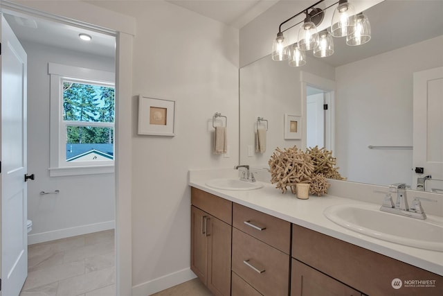 full bathroom featuring double vanity, baseboards, toilet, and a sink