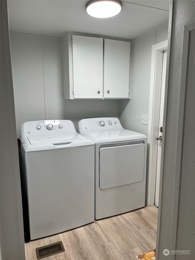 washroom featuring cabinet space, visible vents, light wood finished floors, and washing machine and clothes dryer